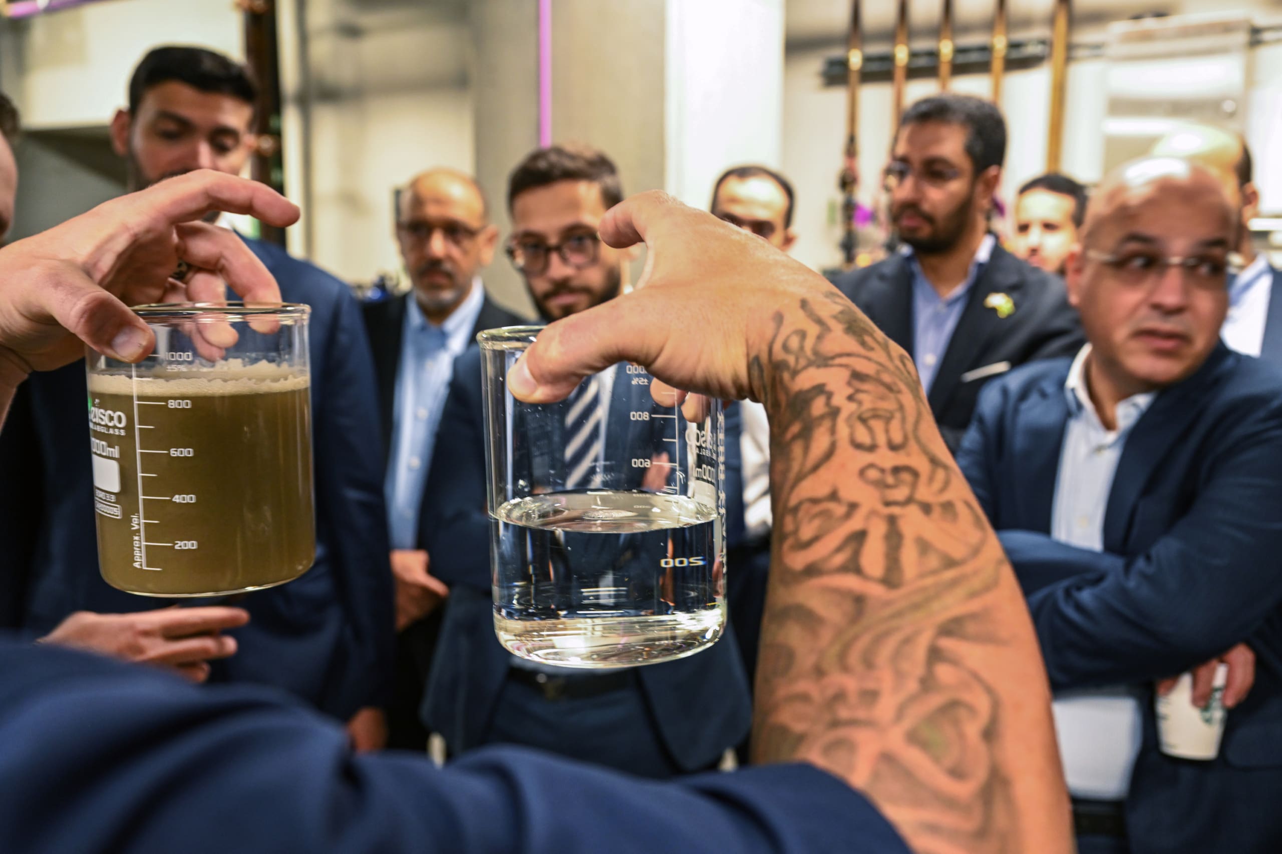Epic operator, Ryan, holding two beakers; one has wastewater before treatment, the other has a sample of crystal clear water in it after treatment from Epic's technology